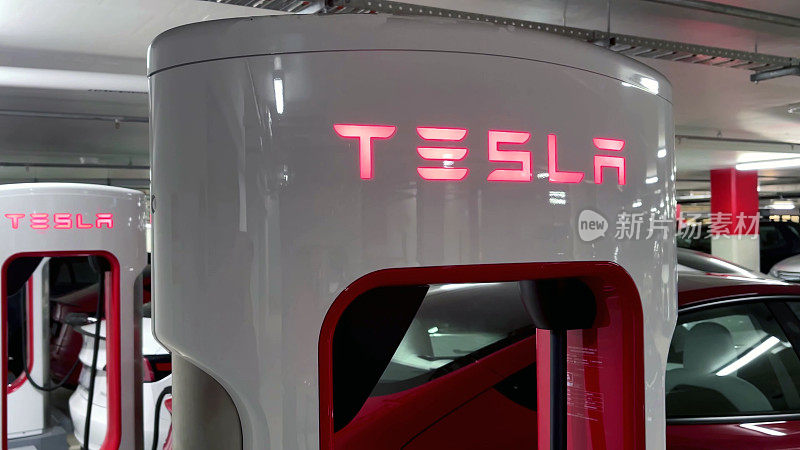 特斯拉增压器(Tesla Supercharger)在一栋建筑的停车场为两辆红色特斯拉Model 3和一辆白色特斯拉Model 3充电。